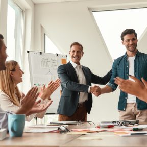 Good job! Two cheerful colleagues shaking hands and smiling while having a meeting in the modern office. Teamwork